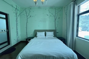 Un dormitorio con cama, mesita de noche, ventana y pared decorada con motivos de árboles.
