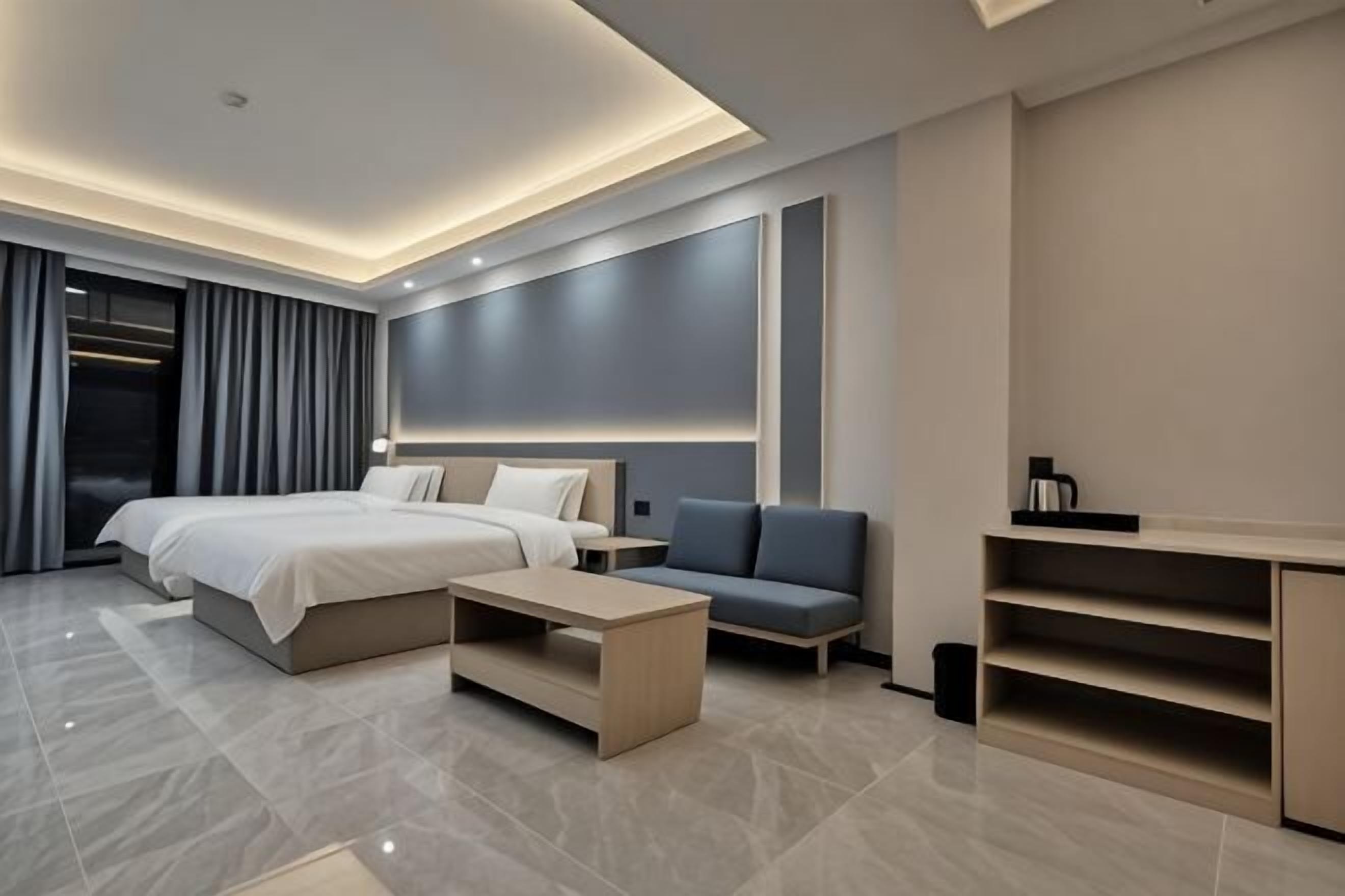 A modern hotel room with a large bed, a sofa, a coffee table, and a desk.