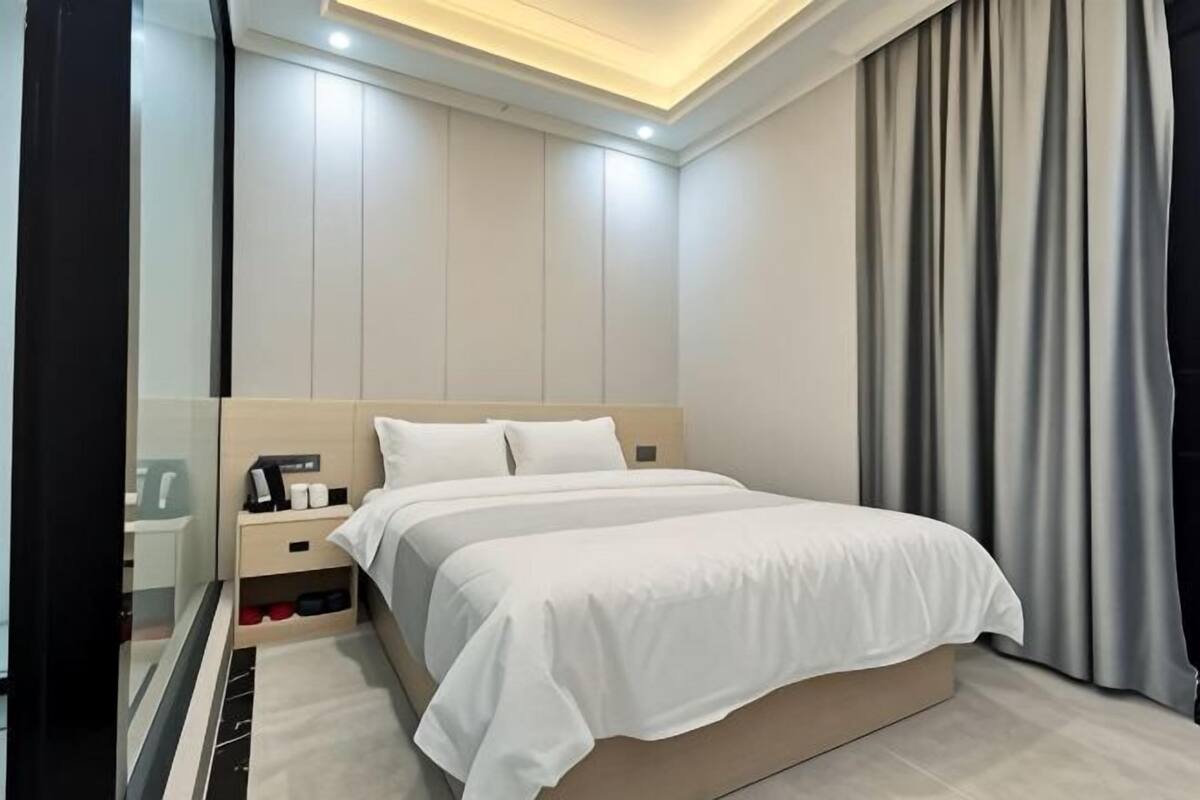 Moderni hotellihuone, jossa on suuri sänky, yöpöydät, yövalaisin ja kattovalaisin.