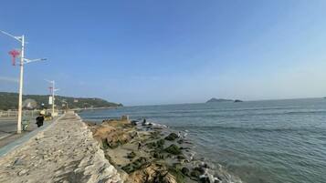 Un paseo marítimo con muro de piedra, cielo despejado y mar en calma.