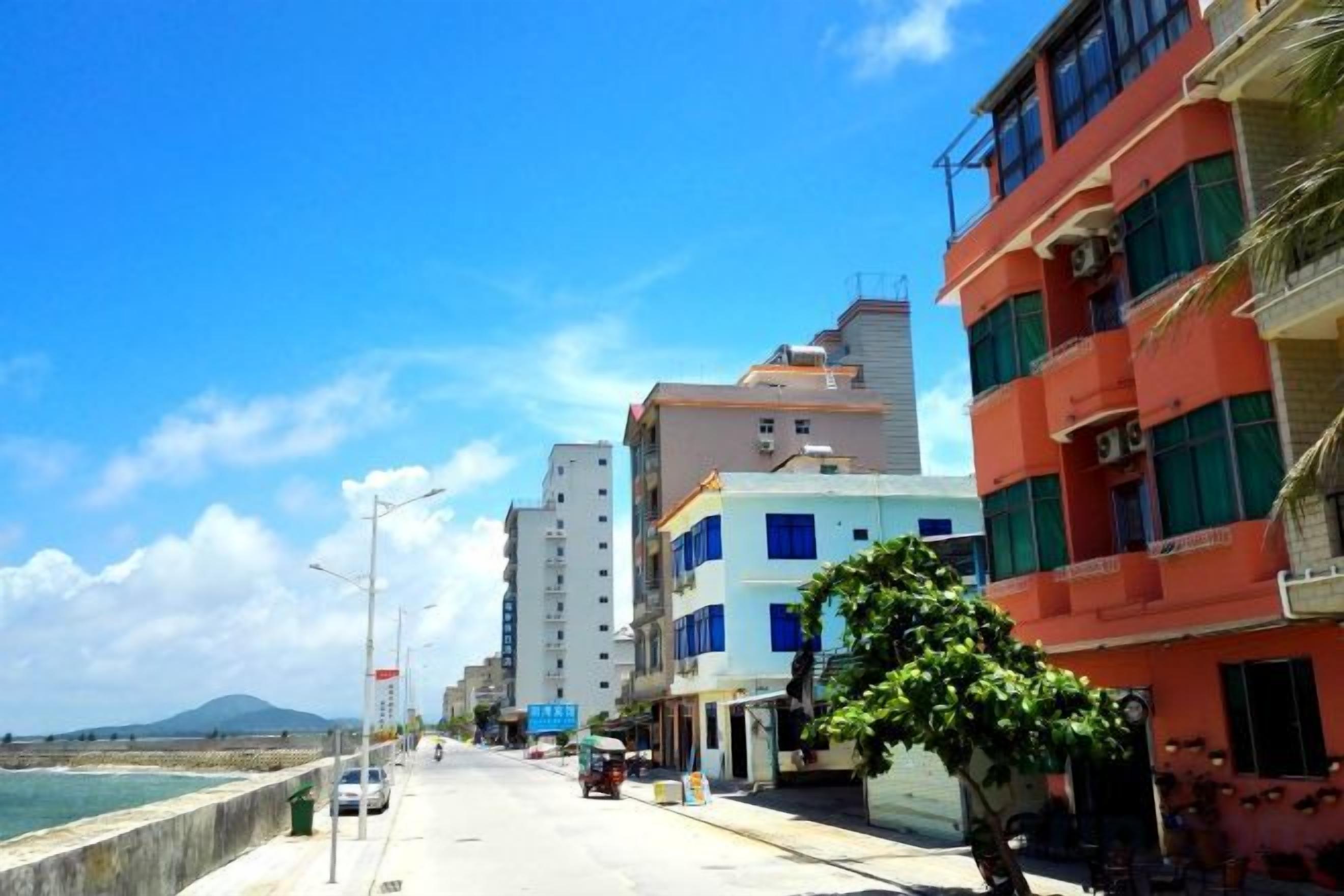 A coastal street with buildings, a clear sky, and a view of the sea.