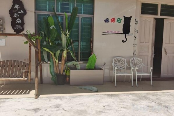 Fachada de un edificio con un mural de un gato, plantas en macetas y dos sillas blancas en el exterior.