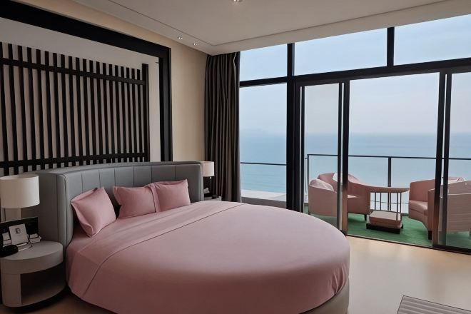 Una cama grande con cabecera, mesitas de noche con lámparas y vistas al mar a través de amplios ventanales.