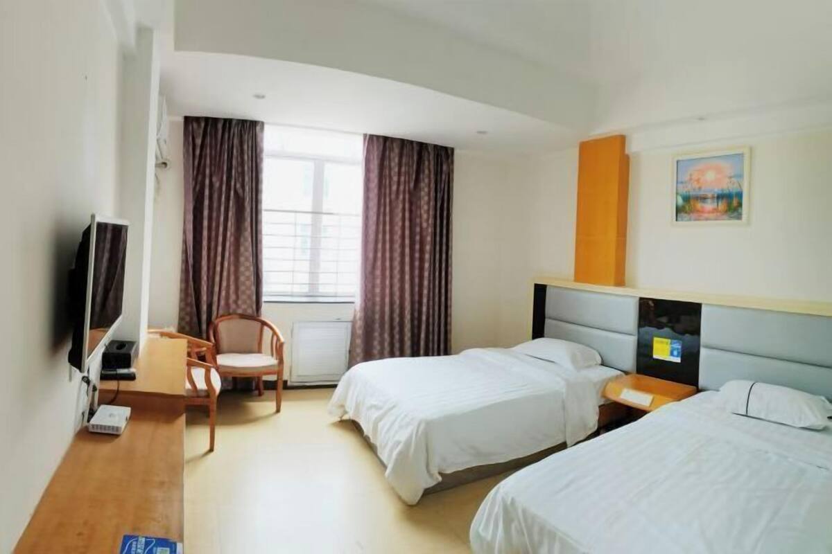 Hotellihuone, jossa on kaksi sänkyä, työpöytä, tuoli, televisio ja ikkuna, jossa on verhot.