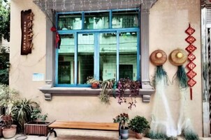 Fachada de edificio con ventana, plantas en macetas, banco y adornos.
