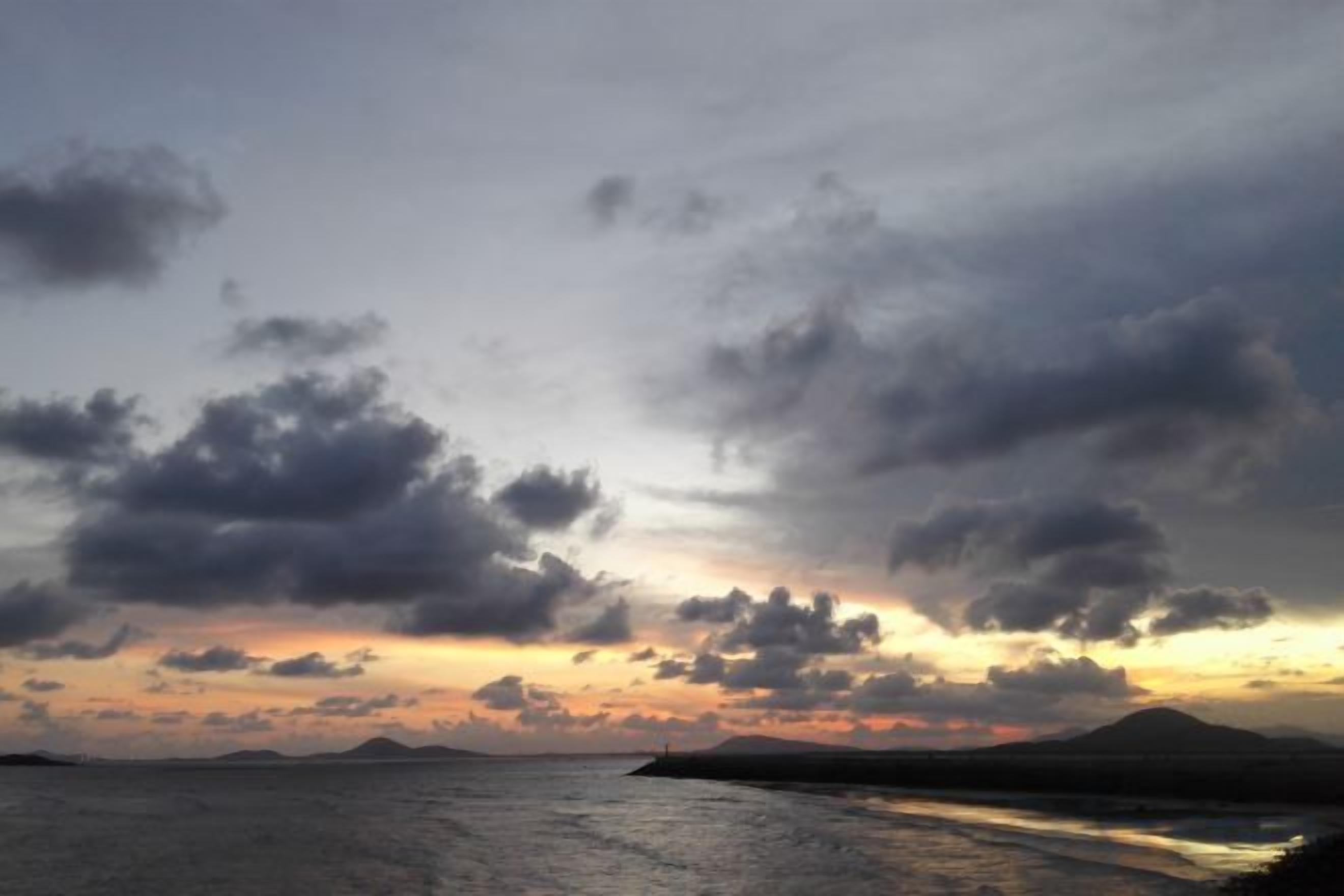 A sunset over a body of water with clouds in the sky.