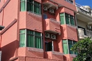 Un edificio de varios pisos con balcones, unidades de aire acondicionado y un ventanal con cortinas.