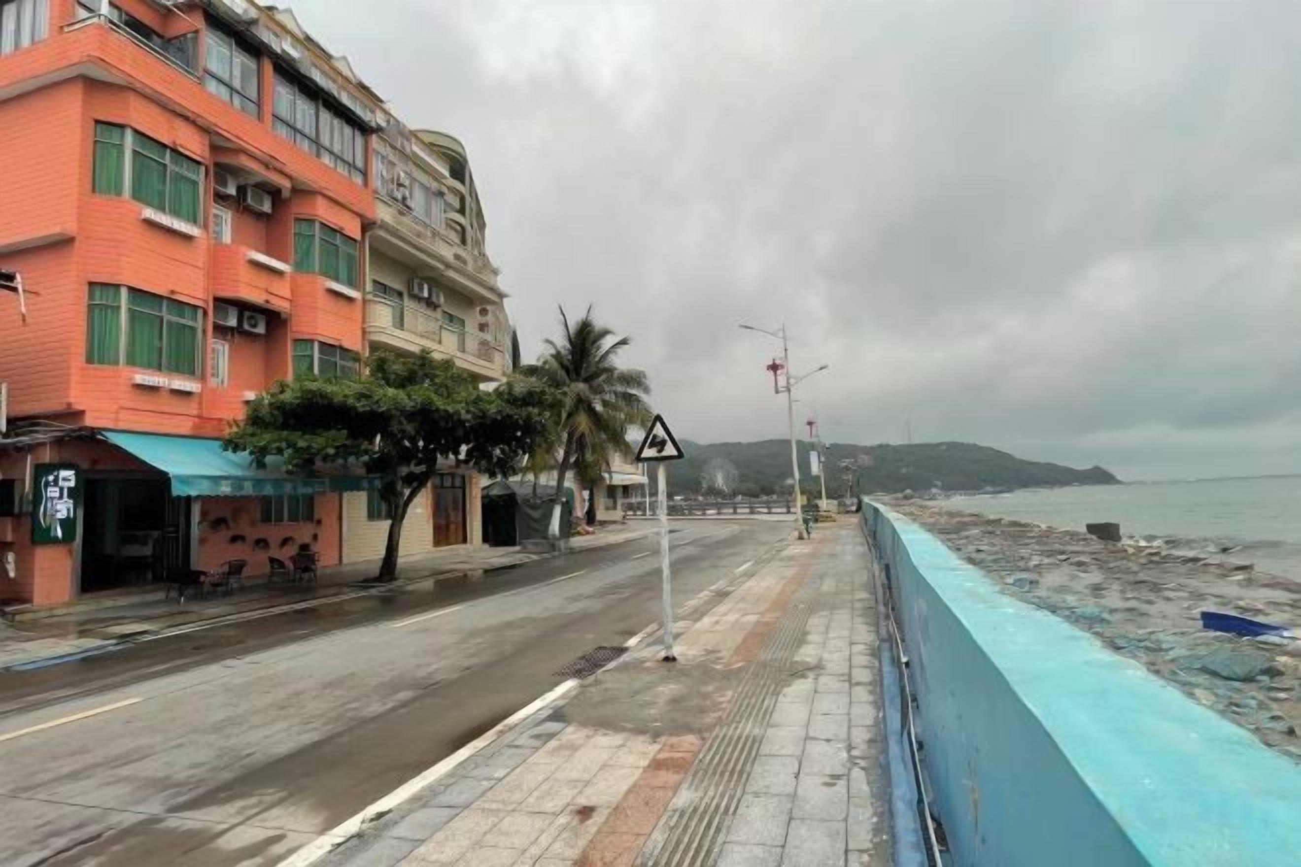 Una strada costiera con edifici, una ringhiera blu e una spiaggia sullo sfondo.