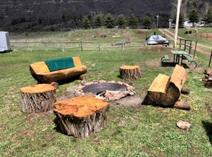 A rustic outdoor seating area with a fire pit, wooden benches, and a picnic table. - Unique Steampunk Tiny House Rental in Swan Valley, Idaho near Jackson Hole (Irwin)