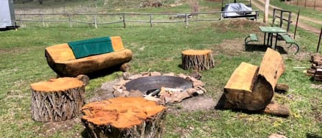 A rustic outdoor seating area with a fire pit, wooden benches, and a picnic table.