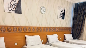 Een hotelkamer met vier eenpersoonsbedden, een houten hoofdbord met bloemenmotieven, een klok en decoratieve wandkunst.