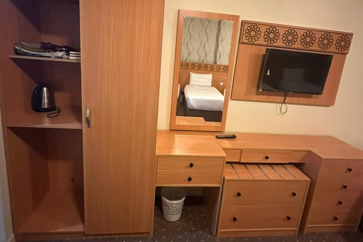 Ein kleines Schlafzimmer mit Holzschrank, Spiegel, Bett und Fernseher.