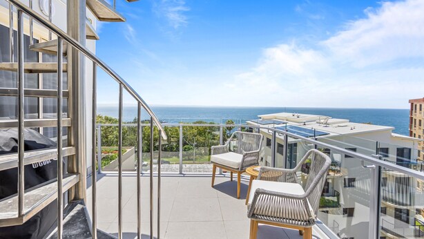 Ein Balkon mit Blick auf das Meer, Korbstühle und ein Grill.