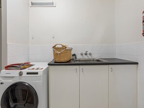 Un área de lavandería con lavadora, un lavabo y una cesta en la encimera.