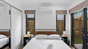 A modern hotel room with a large bed, two bedside tables with lamps, a wooden headboard, and a sliding glass door leading to an outdoor area. - Riverside 3-bed Home With Study Nook and BBQ (Murrumba Downs)