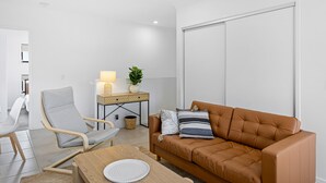 A modern living room with a brown leather sofa, a grey armchair, a wooden coffee table, and a small side table with a lamp and plant. - Riverside 3-bed Home With Study Nook and BBQ (Murrumba Downs)