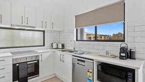 A modern kitchen with white cabinets, a built-in oven, a dishwasher, a microwave, and a window with a view of buildings. - Riverside 3-bed Home With Study Nook and BBQ (Murrumba Downs)