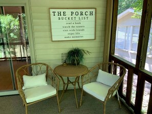 A porch with wicker chairs, a small table, and a sign listing activities like reading a book and visiting with friends.