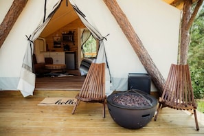 A tent with a kitchen area visible through the entrance, a fire pit, and two wooden chairs. - Gorgeous Safari Tent with Sauna Perfect for a Couple Retreat in Kentucky (Cadiz)
