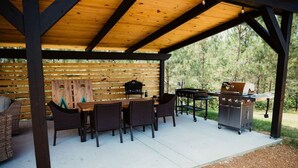 An outdoor patio with a wooden table and chairs, a grill, and a wooden wall with horizontal slats.