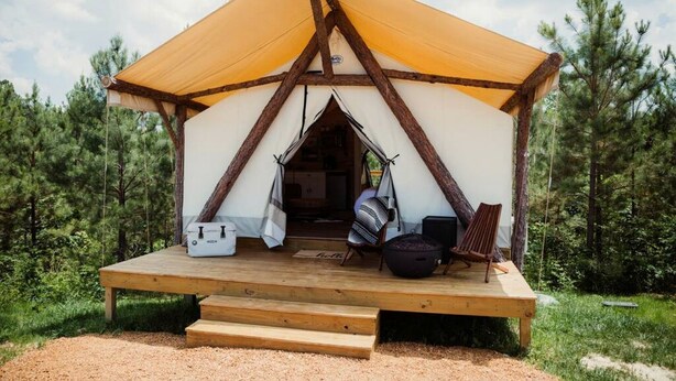 A tent with a wooden deck, a hanging chair, a black bag, and a white object on the ground.