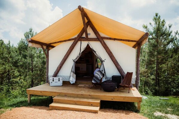 A tent with a wooden deck, a hanging chair, a black bag, and a white object on the ground.