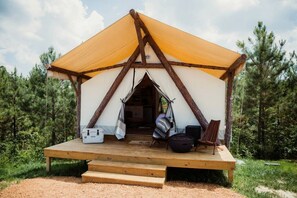 Ein Zelt mit einer Holzterrasse, einem Hängestuhl, einer schwarzen Tasche und einem weißen Gegenstand am Boden.