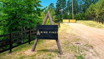 A sign for 'Nine Pines' with a wooden fence and trees in the background.