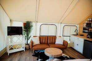 Un espacio habitable compacto con sofá, televisión, área de cocina y una planta en maceta.