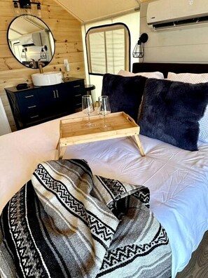 Ein Schlafzimmer mit einem Bett, einem Nachttisch aus Holz mit Gläsern, einem Spiegel, einem Fenster und einer Wand-Klimaanlage.