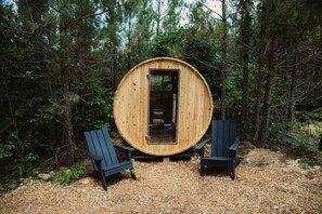 Un sauna en bois situé dans une forêt, avec deux fauteuils Adirondack.