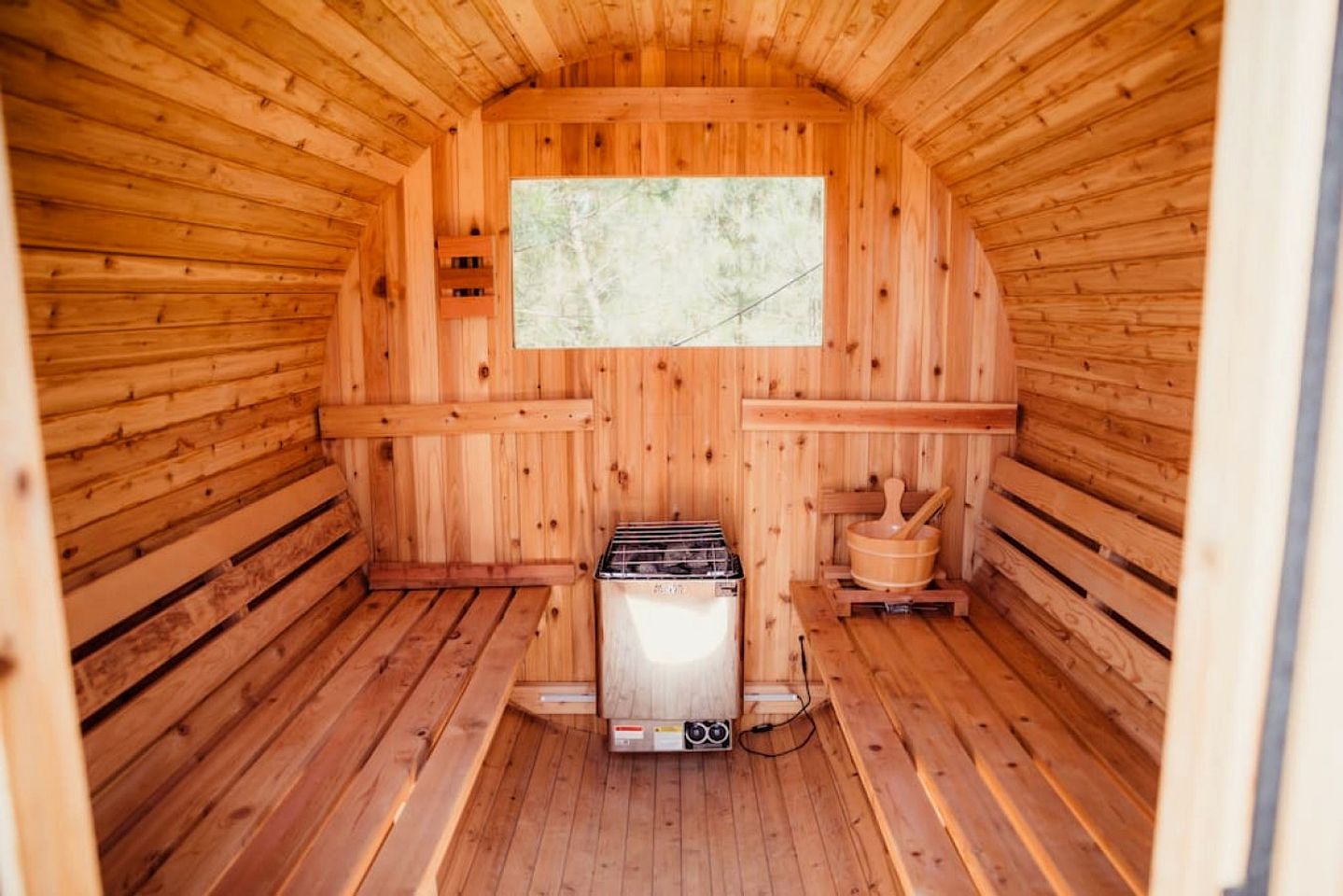 A wooden cabin interior with a stove, a window, and a wooden bench.