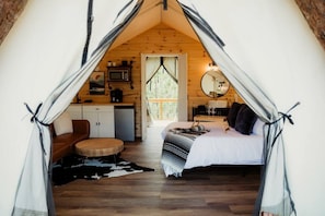 A cozy tented accommodation with a bed, a small seating area, a desk, and a mirror. - Gorgeous Safari Tent with Sauna Perfect for a Couple Retreat in Kentucky (Cadiz)