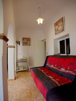 A room with a red sofa, a small table with books, a wall-mounted light fixture, and a door. - Casa Paraíso Natural: naturaleza y relax en Gran Canaria (Las Lagunetas)
