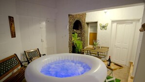 Une pièce avec un jacuzzi, un banc en bois, une table avec une bouteille et un verre, et une décoration en forme de papillon au mur.