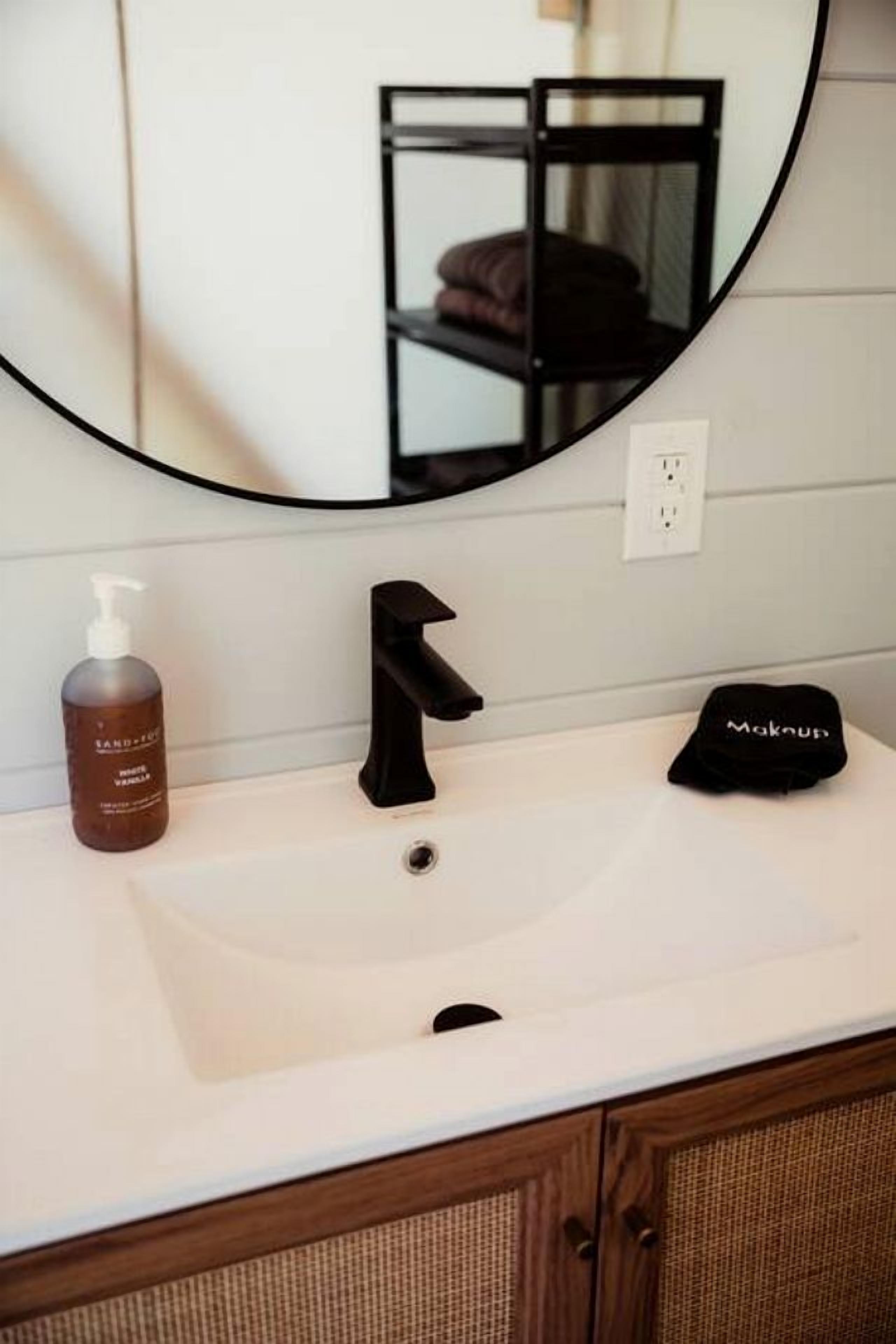 Une salle de bain avec un lavabo blanc, un robinet noir, un flacon de savon liquide et un bouchon noir posé sur le comptoir.