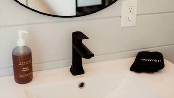 Une salle de bain avec un lavabo blanc, un robinet noir, un flacon de savon liquide et un bouchon noir posé sur le comptoir.