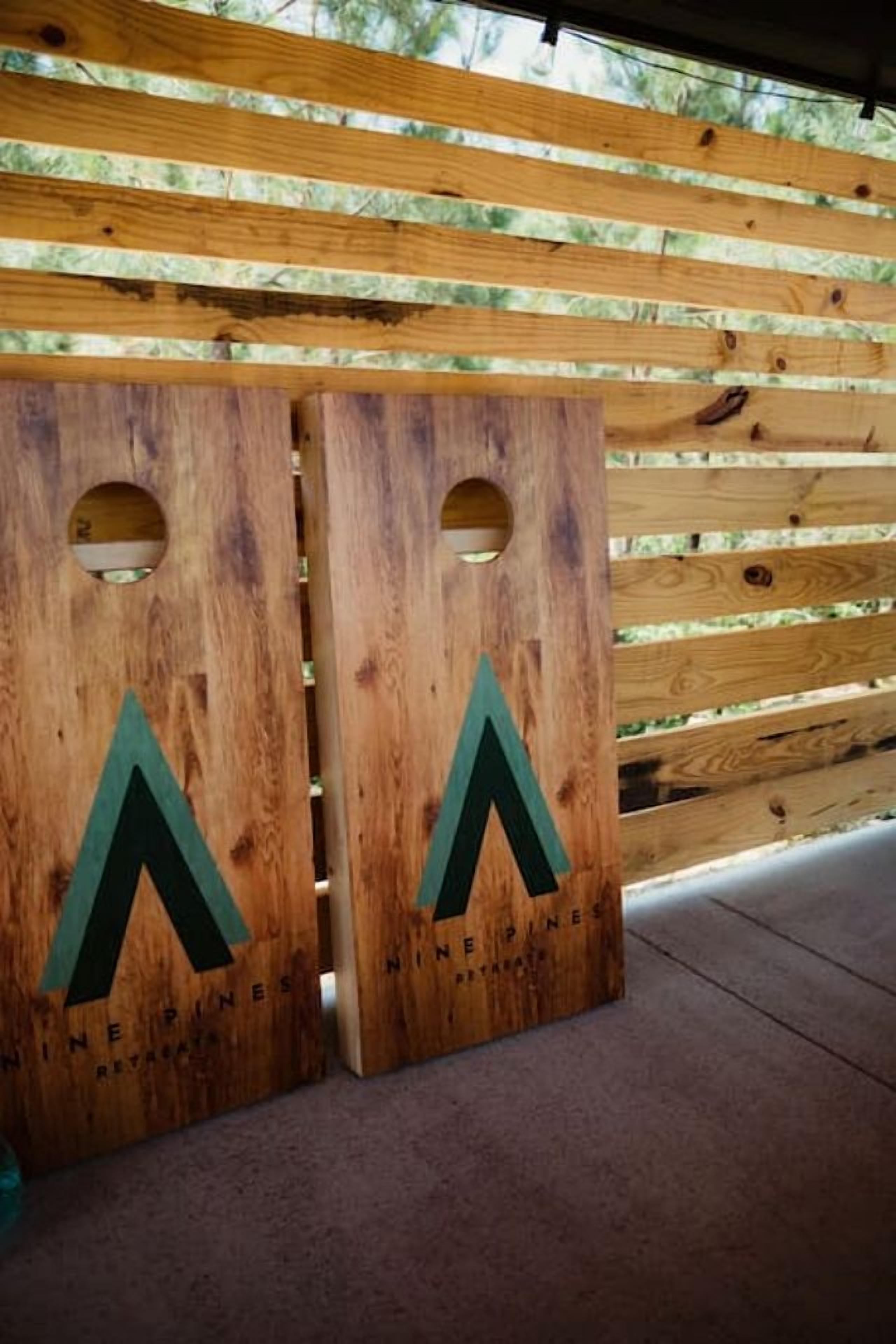 Deux panneaux en bois, ornés d’un logo et d’un texte, sont posés sur un sol en béton, adossés à une clôture en bois.