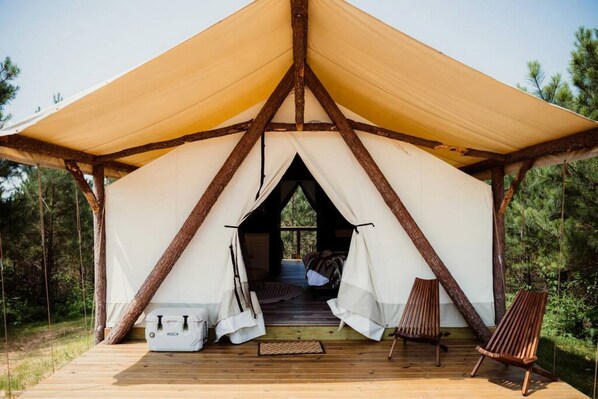 Une tente dotée d’une terrasse en bois, d’un lit et de deux chaises.