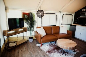 A living area with a TV, sofa, round table, and a potted plant.