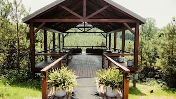 A covered outdoor seating area with tables and chairs, surrounded by greenery.