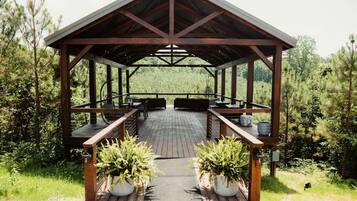 A covered outdoor seating area with tables and chairs, surrounded by greenery.