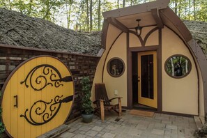 A small, rustic cabin with a wooden door, a circular window, and a bench outside.