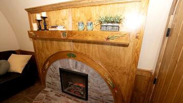 A fireplace with a brick surround, a wooden mantel above it, and a shelf with decorative items.