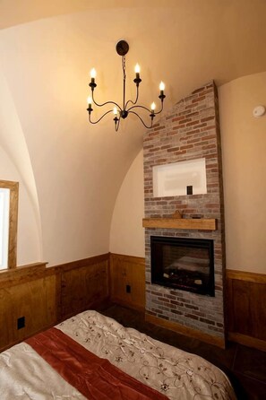 A bedroom with a brick fireplace, a chandelier, and a bed with a floral bedspread.