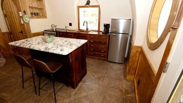 A kitchen with a marble island, wooden cabinets, a stainless steel refrigerator, and a tiled floor.