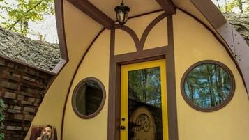 A unique, curved building with a yellow door and circular windows, surrounded by trees.