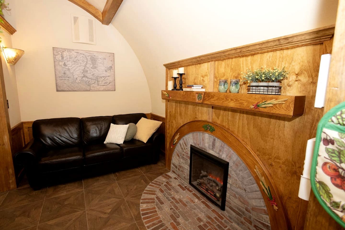 A living room with a fireplace, a black leather sofa, and a wooden mantelpiece with decorative items.