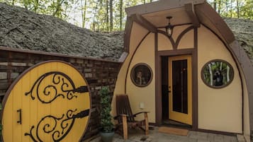 A small, rustic cabin with a wooden door, a circular window, and a bench outside.