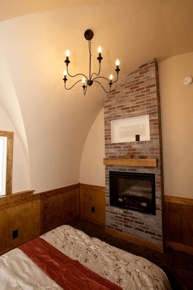 A bedroom with a brick fireplace, a chandelier, and a bed with a floral bedspread.